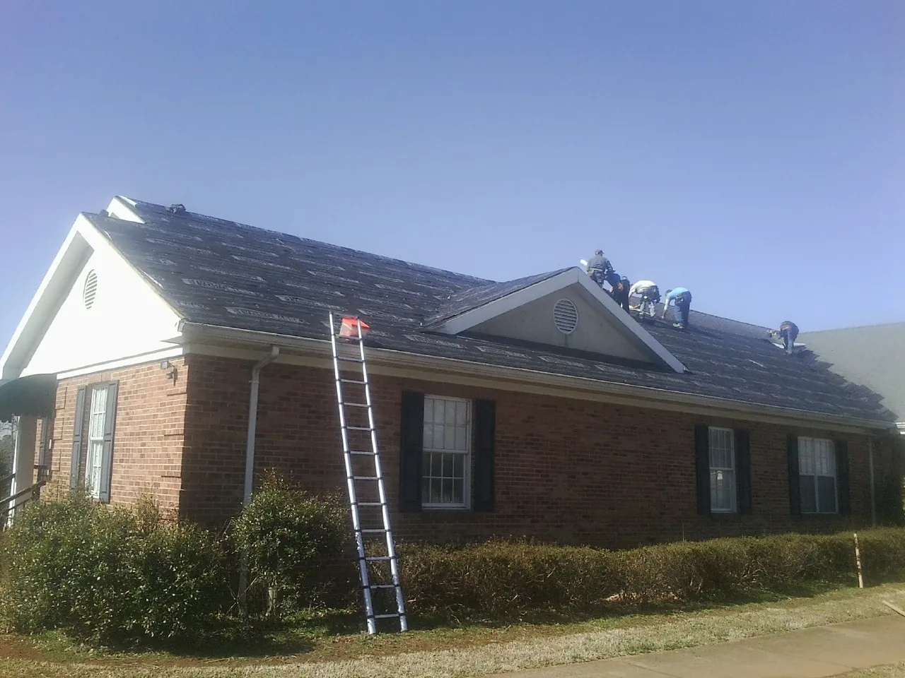 Crew tearing shingles off a brick ranch roof with a ladder set — Emergency Roof Repair work by our crew in Albert