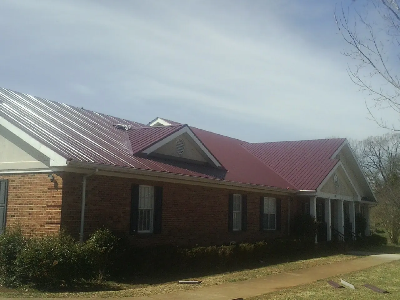 Red metal roof with gabled entries on a long brick building, from a Hail Damage Roof Repair job in Albert