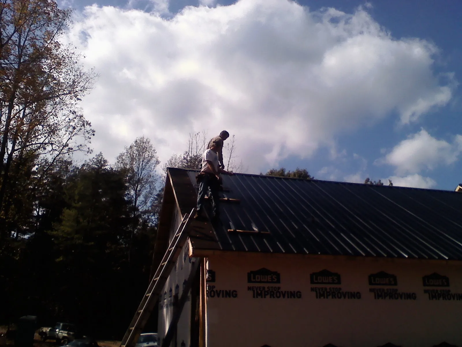 Roofer fastening dark metal panels high against a cloudy sky, from a Roof Inspection job in Albert